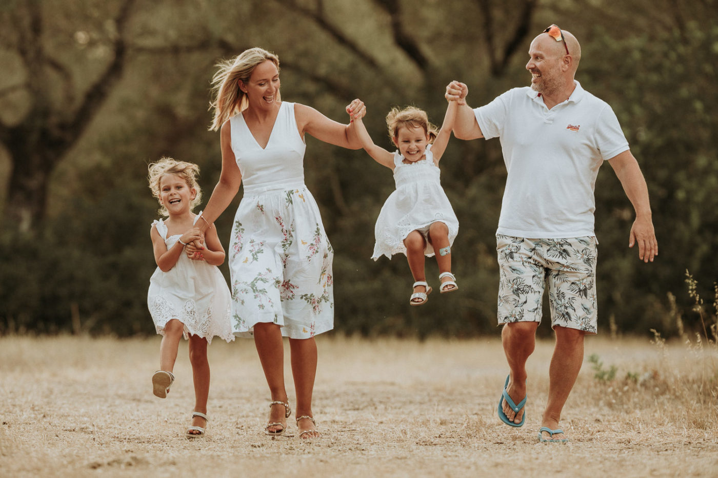 Die Eltern und ihre zwei hübsche Mädchen laufen während des Foto Shootings auf Mallorca hüpfend auf die Kamera zu